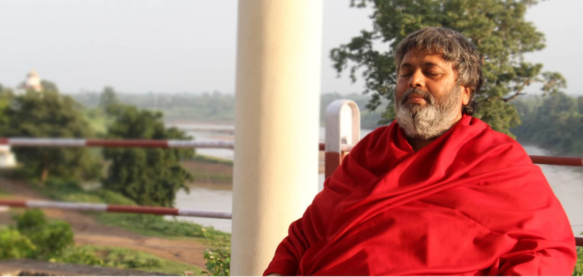 Dr. Avdhoot Shivanand seated in meditation on a riverside veranda
